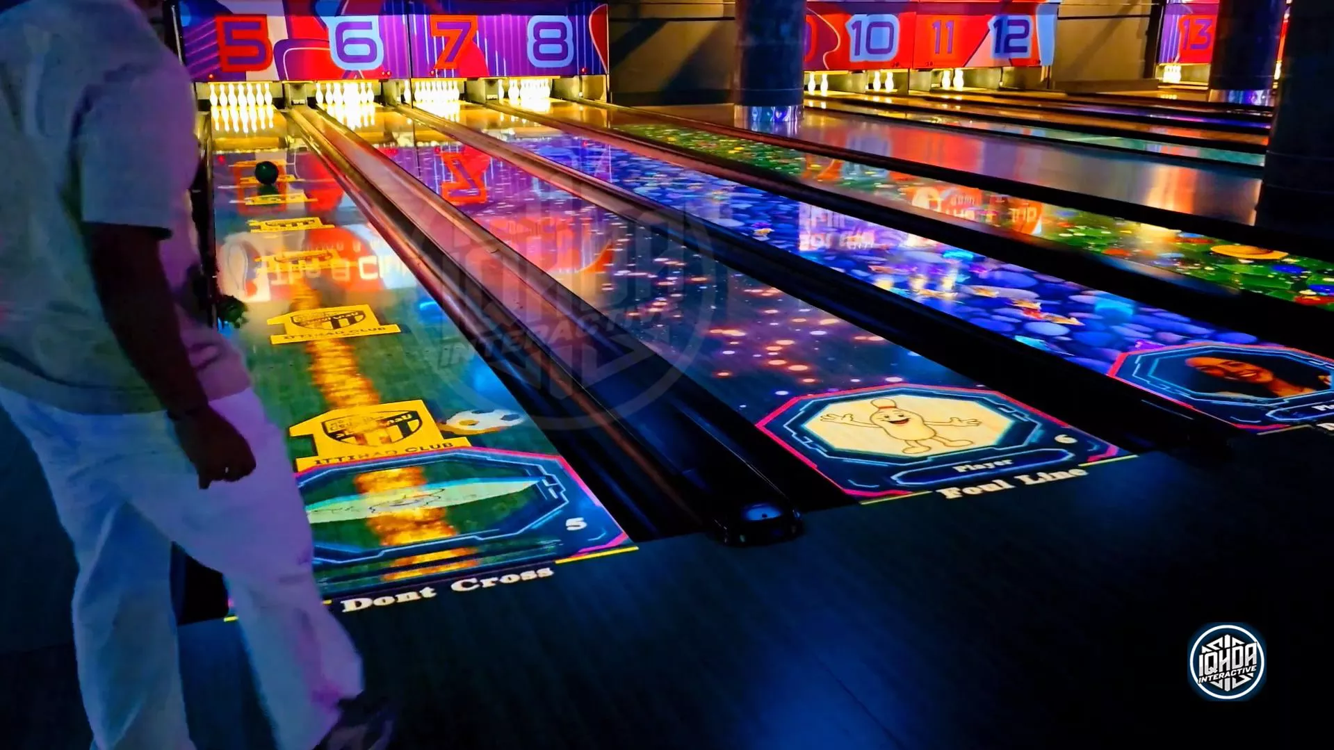 Player throws a bowling ball with real-time projection tracking on lane 5, showing 13 IQHDA Interactive AR bowling lanes with unique game themes